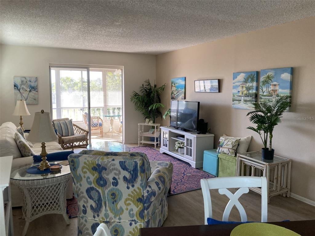 A living room features a patterned armchair, a white media console, and a glass-enclosed balcony — 304 47TH AVENUE DRIVE W UNIT 307, BRADENTON, FL