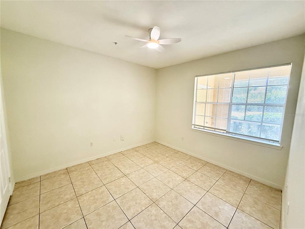 An empty room features light-colored tile flooring, white walls, a ceiling fan, and a window — 2674 ROBERT TRENT JONES DRIVE UNIT 312, ORLANDO, FL