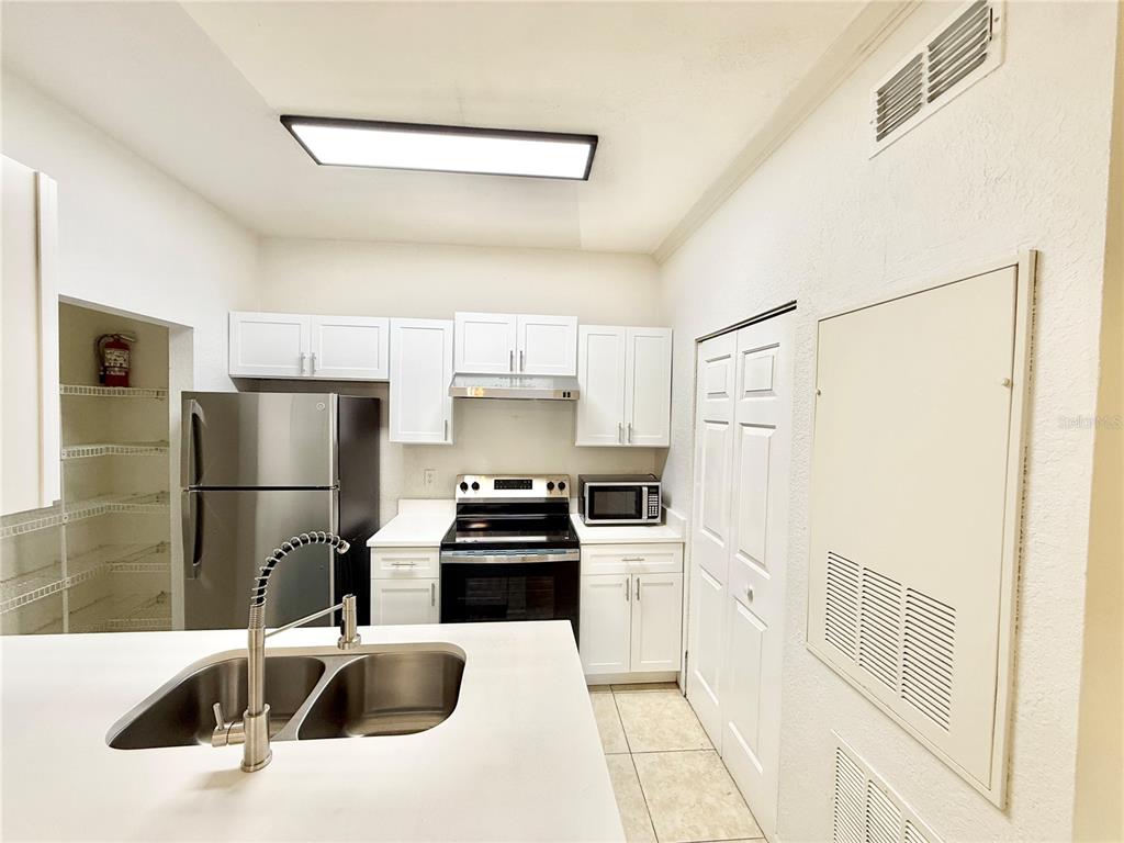 A kitchen features white cabinets, stainless steel appliances, a double sink, and a pantry closet — 2674 ROBERT TRENT JONES DRIVE UNIT 312, ORLANDO, FL