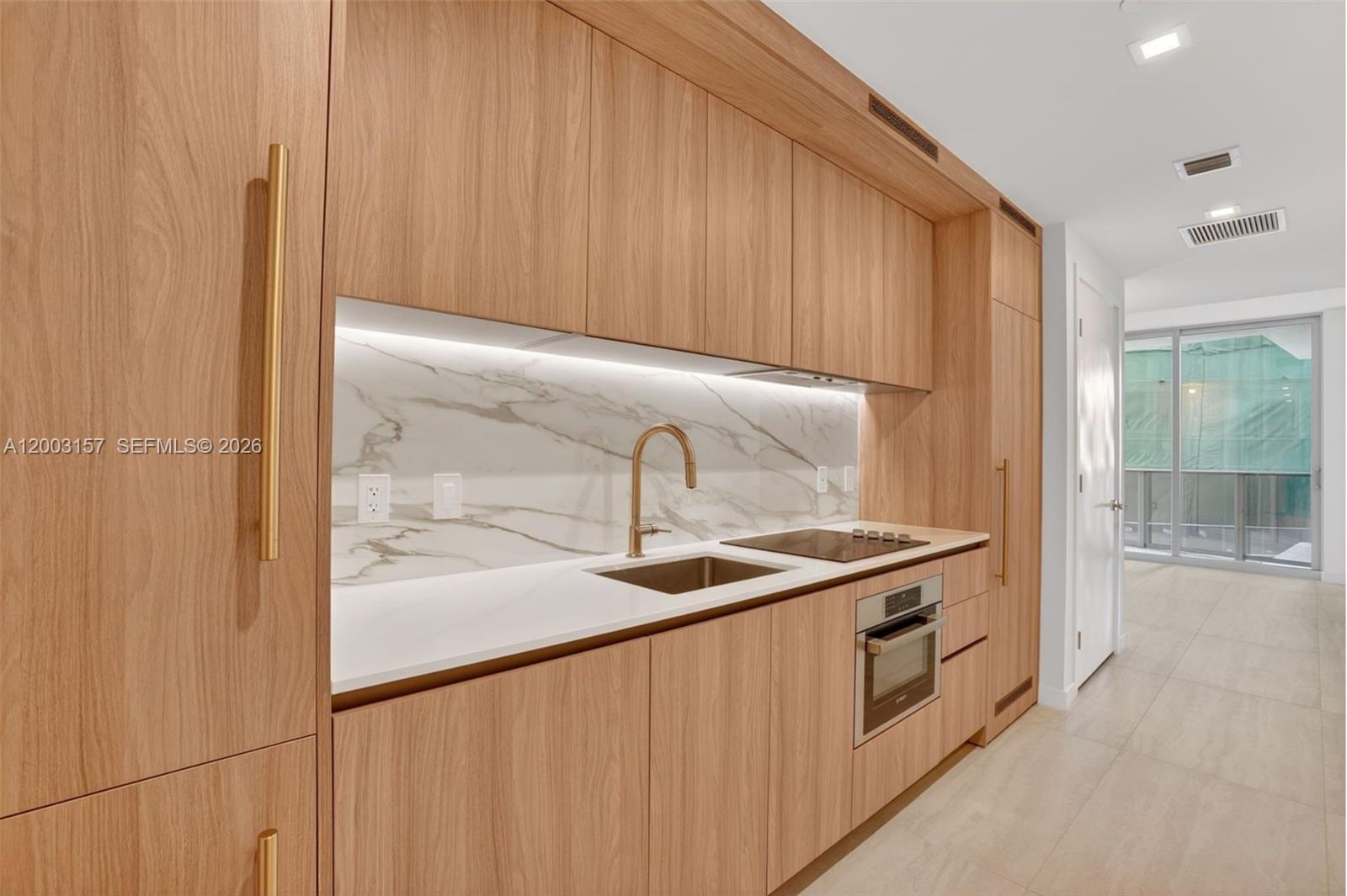 A modern kitchen features light wood cabinetry, white marble backsplash, and gold-toned hardware — 77 SE 5th St # 2705, Miami FL 33131, MIAMI, FL