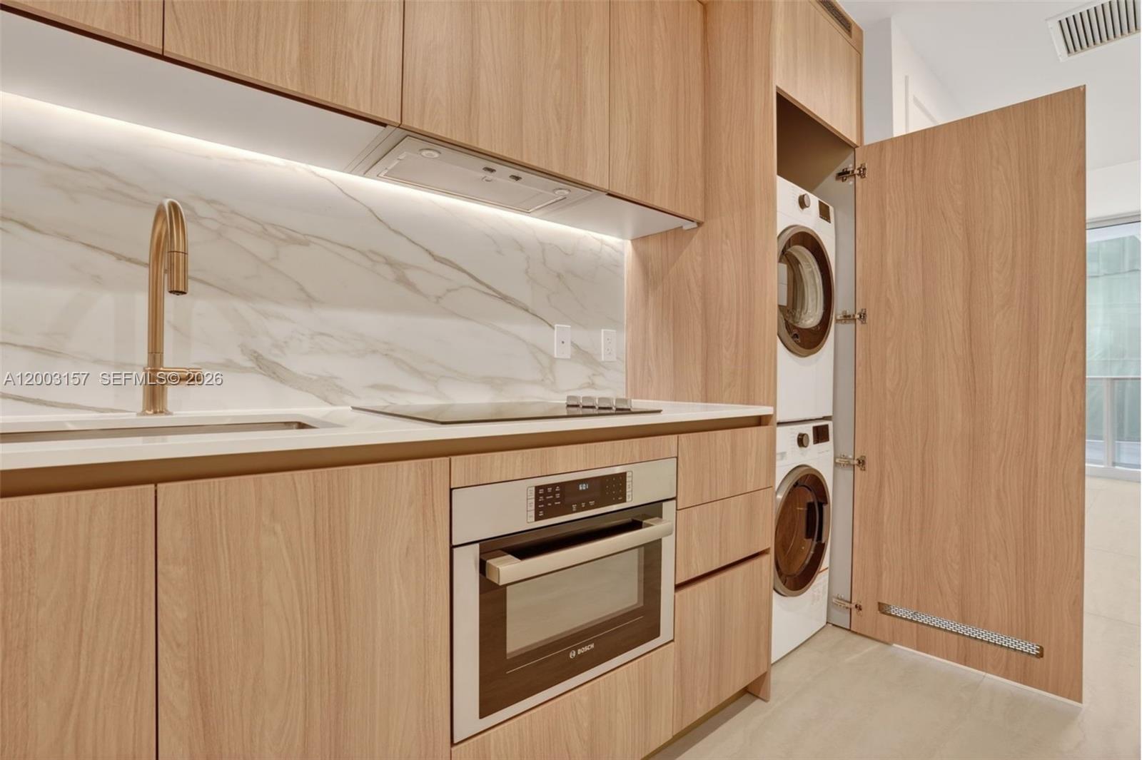 A modern kitchen features light wood cabinetry, a marble backsplash, and a stacked laundry unit — 77 SE 5th St # 2705, Miami FL 33131, MIAMI, FL