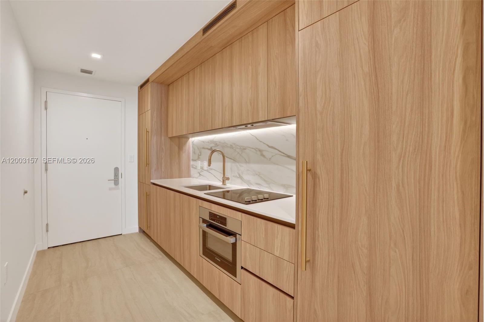 A modern kitchen features light wood cabinetry, a marble backsplash, and integrated stainless steel appliances — 77 SE 5th St # 2705, Miami FL 33131, MIAMI, FL