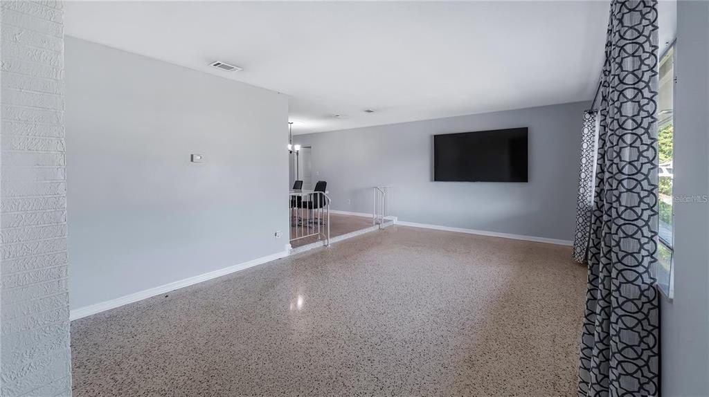 A spacious living room features light gray walls, terrazzo flooring, and a wall-mounted television — 2612 TIMBERLAKE DRIVE, ORLANDO, FL