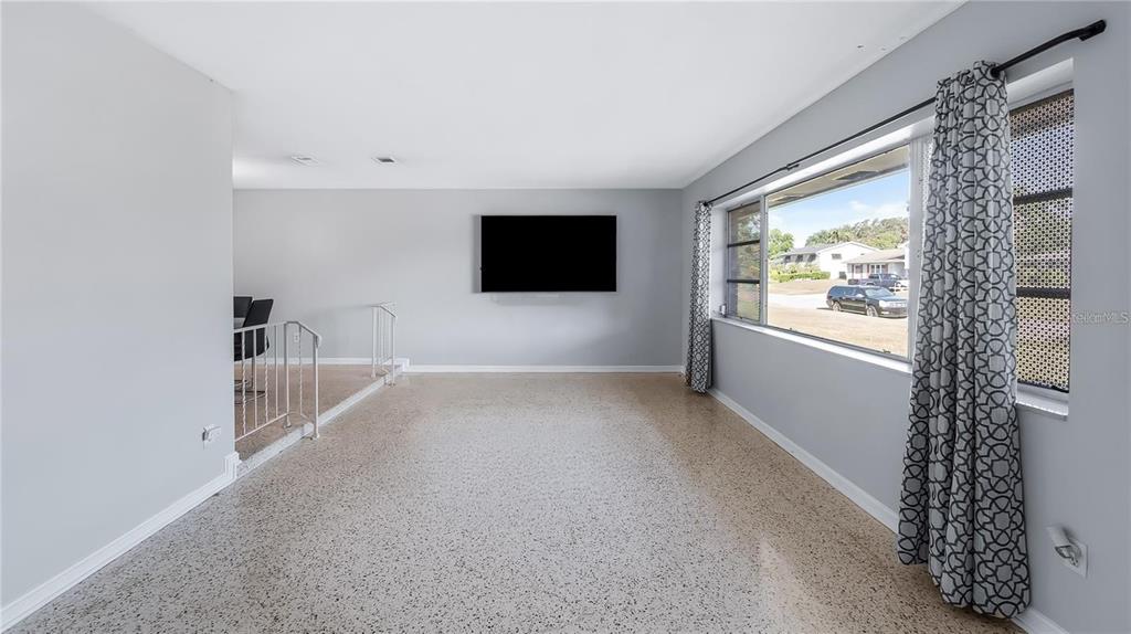 A living room with light gray walls, terrazzo flooring, a wall-mounted television, and large windows — 2612 TIMBERLAKE DRIVE, ORLANDO, FL