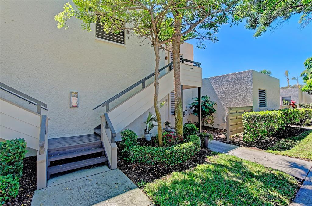 Exterior view of a multi-story building with wooden stairs leading to an upper-level entrance — 144 PINEHURST DRIVE UNIT 144, BRADENTON, FL
