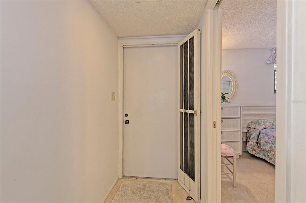A white front door with a screen door opens into a hallway beside a bedroom — 144 PINEHURST DRIVE UNIT 144, BRADENTON, FL