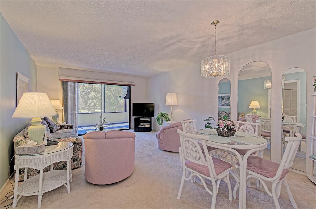 A living and dining area with light carpet, pink armchairs, and a glass-topped dining set — 144 PINEHURST DRIVE UNIT 144, BRADENTON, FL