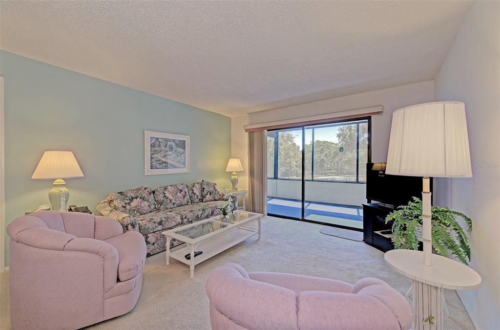 A living room features a floral sofa, two lavender armchairs, and a sliding glass door — 144 PINEHURST DRIVE UNIT 144, BRADENTON, FL