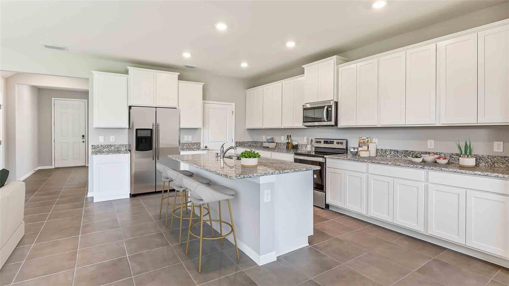 A modern kitchen features white cabinets, granite countertops, a center island, and stainless steel appliances — 3516 HAZY GLEN LANE, PLANT CITY, FL