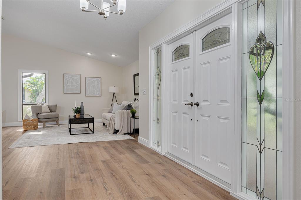 A bright entryway with wood-look flooring leads into a living room with a white sofa — 4415 MARINE PARKWAY, NEW PORT RICHEY, FL