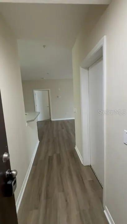 A hallway with wood-look flooring leads toward an open living area with a white door — 5560 METROWEST BOULEVARD UNIT 3-207, ORLANDO, FL