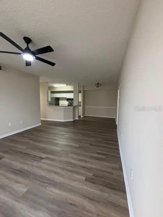 An open-concept living area features wood-look flooring and a ceiling fan, leading to a kitchen — 5560 METROWEST BOULEVARD UNIT 3-207, ORLANDO, FL