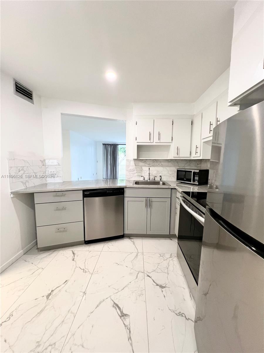A kitchen features white cabinets, stainless steel appliances, marble-patterned countertops, and matching floor tiles — 1710 NE 191st St # 3, Miami FL 33179, MIAMI, FL
