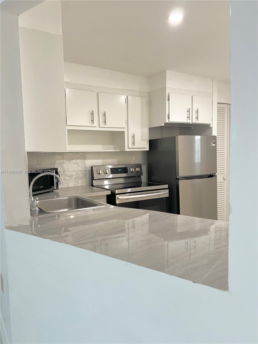 A kitchen features white cabinets, stainless steel appliances, and a gray marble-patterned countertop — 1710 NE 191st St # 3, Miami FL 33179, MIAMI, FL