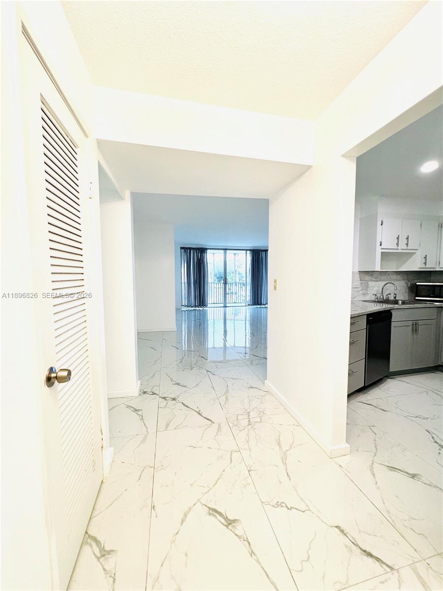 A hallway with white marble-patterned tile floors leads toward a living area with balcony doors — 1710 NE 191st St # 3, Miami FL 33179, MIAMI, FL