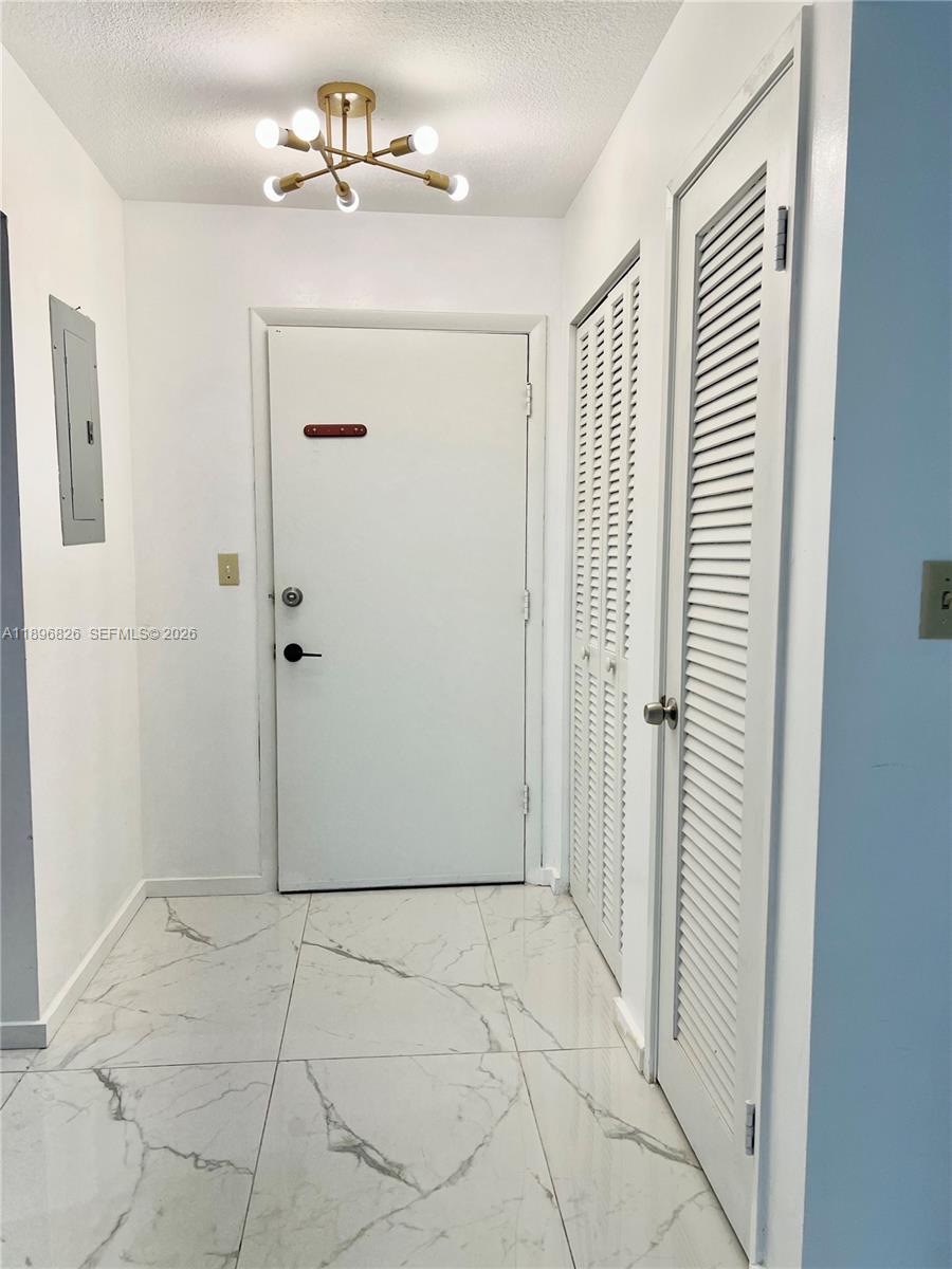 An entryway features white marble-look tile flooring, a modern light fixture, and louvered closet doors — 1710 NE 191st St # 3, Miami FL 33179, MIAMI, FL