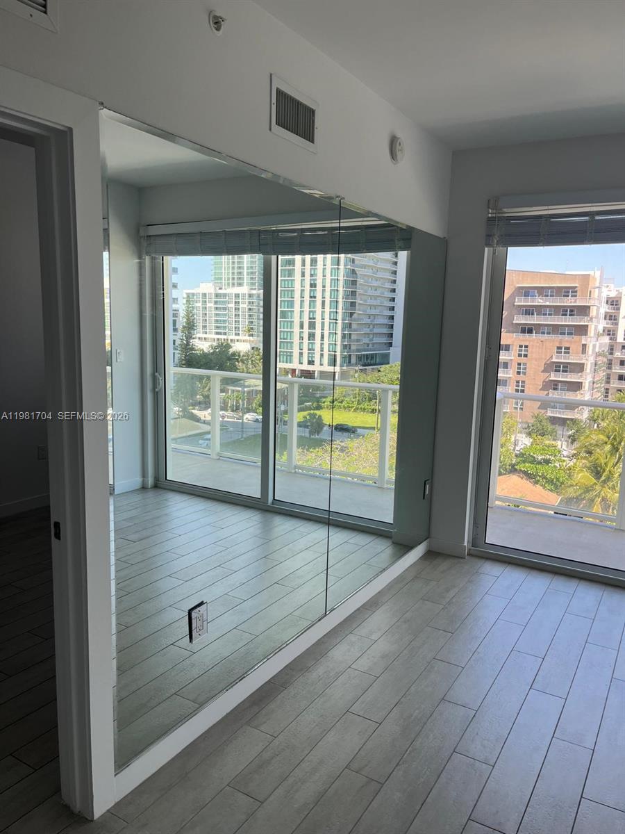A room with light wood-look tile flooring, a large wall mirror, and sliding glass doors — 321 NE 26th St # 717, Miami FL 33137, MIAMI, FL