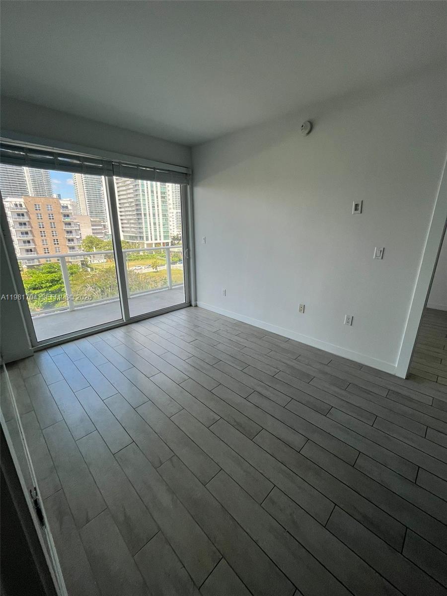 An empty room with light wood-look tile flooring, white walls, and a sliding glass balcony door — 321 NE 26th St # 717, Miami FL 33137, MIAMI, FL