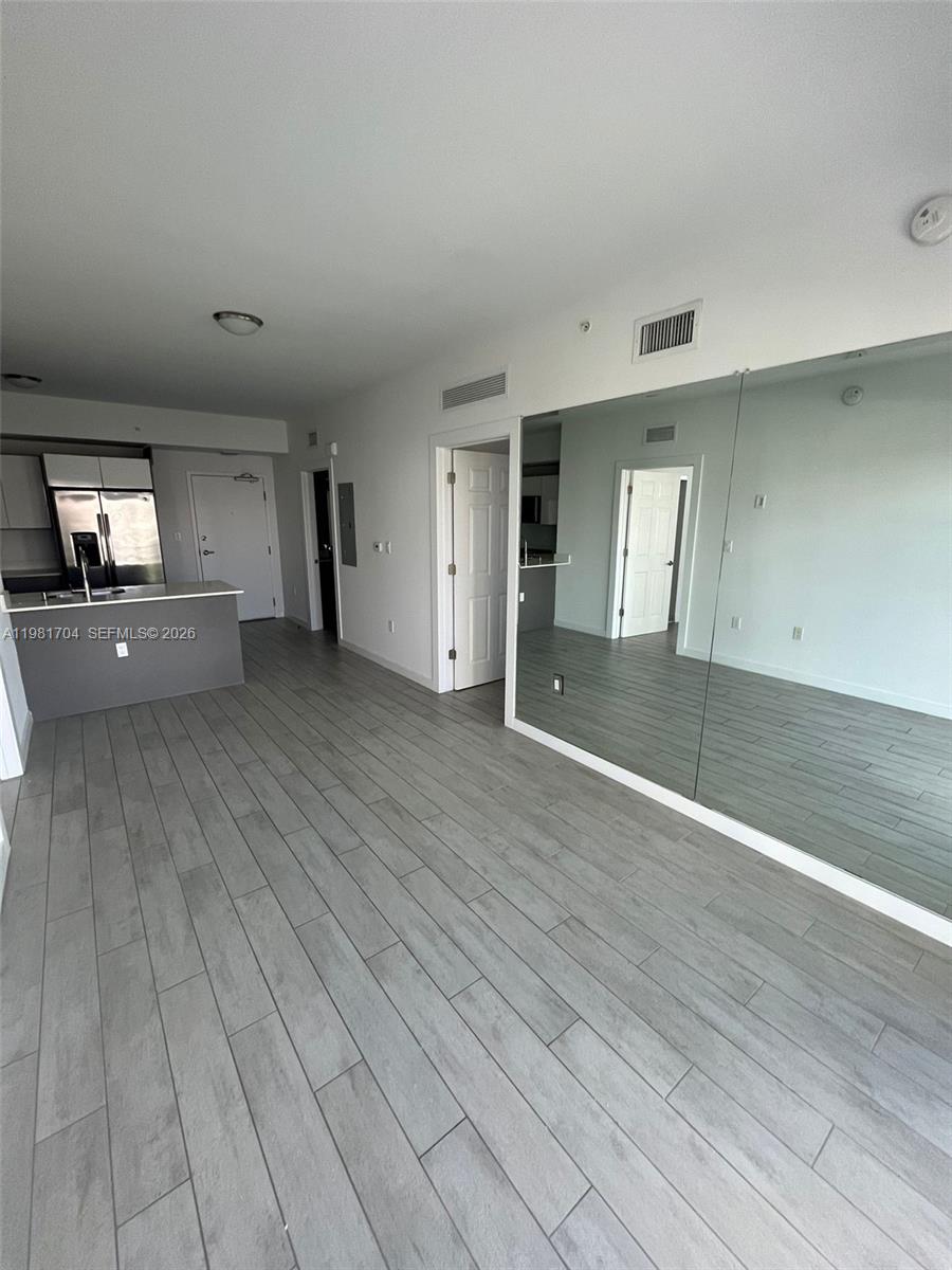 An open-concept living area features gray wood-look tile flooring and a large wall mirror — 321 NE 26th St # 717, Miami FL 33137, MIAMI, FL