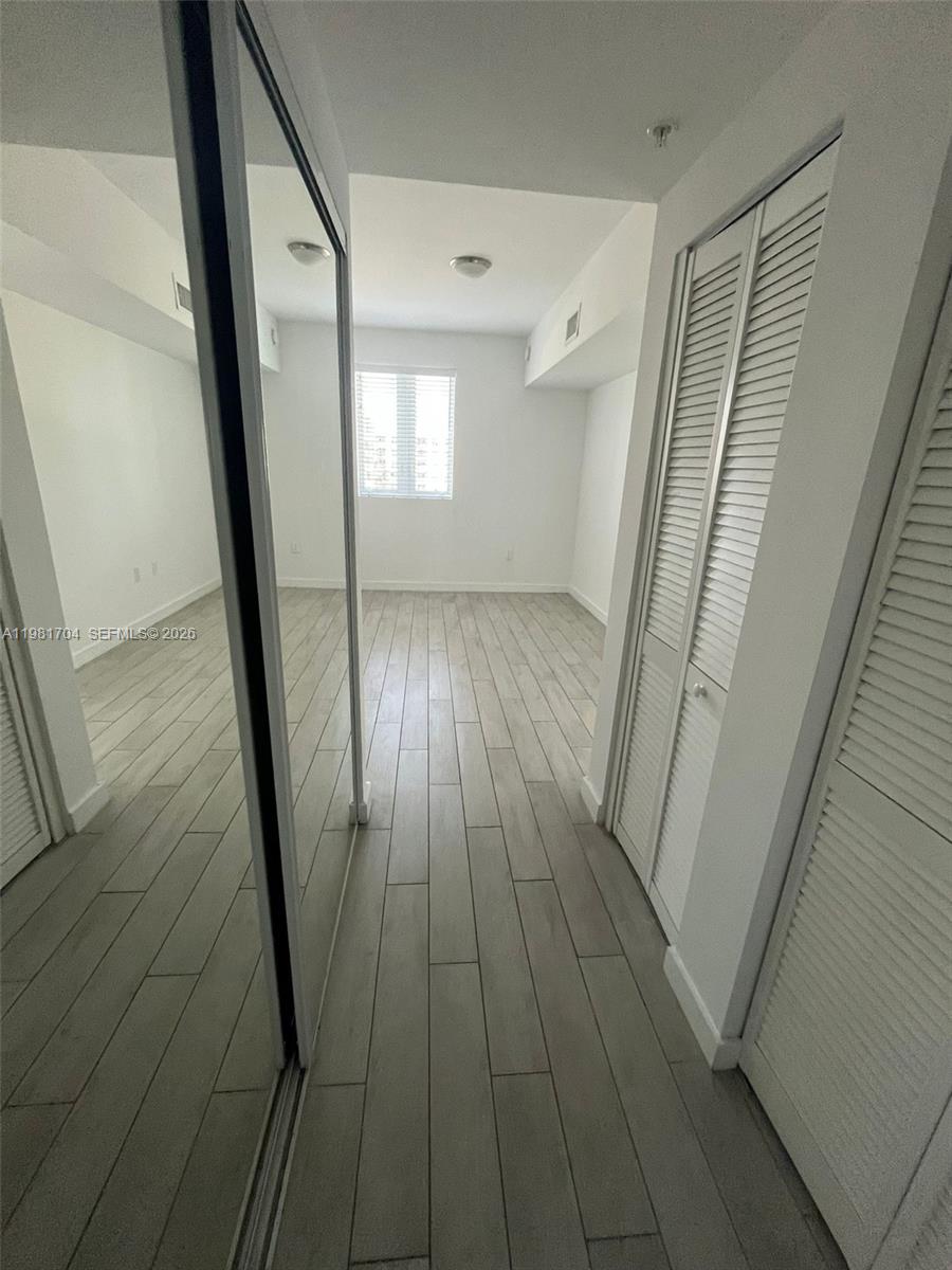 A room with light wood-look tile flooring, mirrored closet doors, and white louvered closet doors — 321 NE 26th St # 717, Miami FL 33137, MIAMI, FL