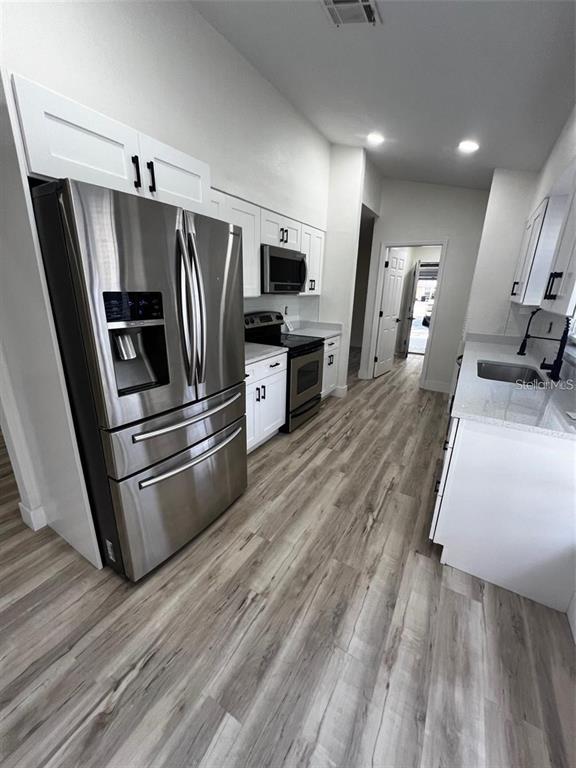 A modern kitchen features white cabinetry, stainless steel appliances, and light wood-look flooring — 339 PEMBROKE LANE S UNIT 228, VENICE, FL