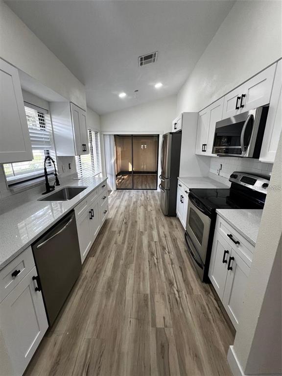 A galley kitchen features white cabinets, stainless steel appliances, and light wood-look flooring — 339 PEMBROKE LANE S UNIT 228, VENICE, FL