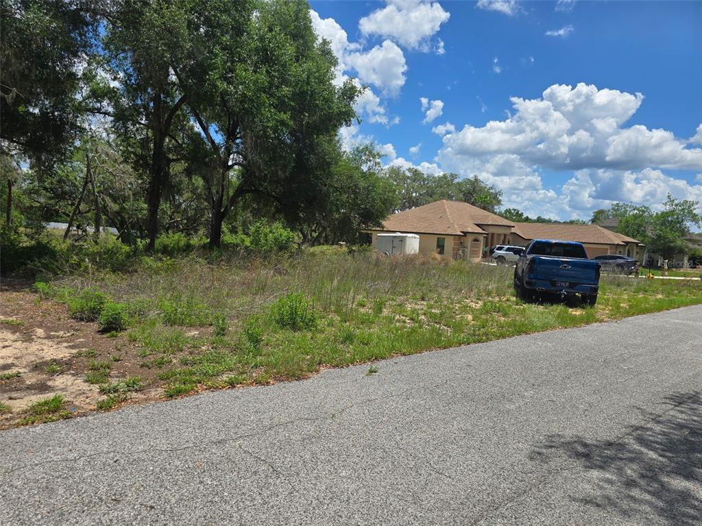 A vacant, grassy lot sits next to a house with a blue truck parked nearby — 5066 WESTLAKE BOULEVARD, DADE CITY, FL