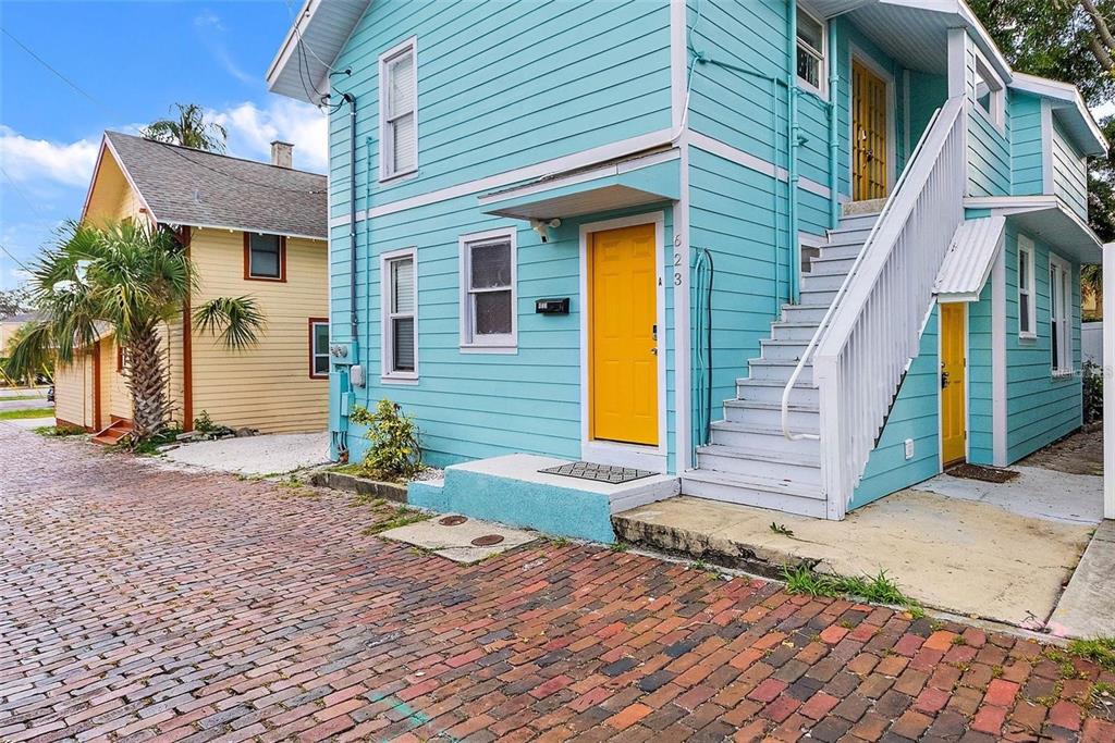 A two-story turquoise house with yellow doors and an exterior staircase sits on a brick street — 623 MOUND PARK WAY S, ST PETERSBURG, FL