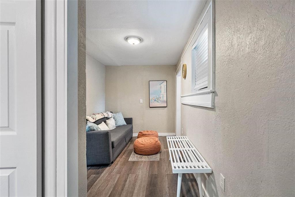 A narrow room features wood-look flooring, a gray sofa, two orange poufs, and a bench — 623 MOUND PARK WAY S, ST PETERSBURG, FL