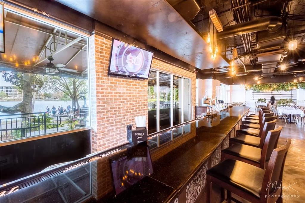 A bar area features a long dark countertop, brick wall, and large windows overlooking a lake — 407 E CENTRAL BOULEVARD, ORLANDO, FL