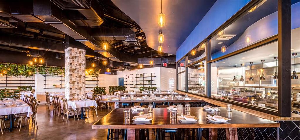 A restaurant interior features dining tables, hanging pendant lights, and an open kitchen behind glass — 407 E CENTRAL BOULEVARD, ORLANDO, FL