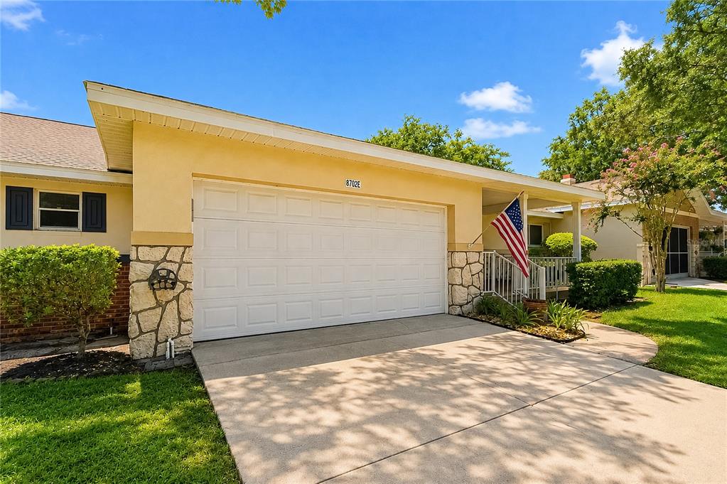 A yellow house exterior features a white garage door, stone accents, and an American flag — 8702 SW 94TH STREET UNIT E, OCALA, FL