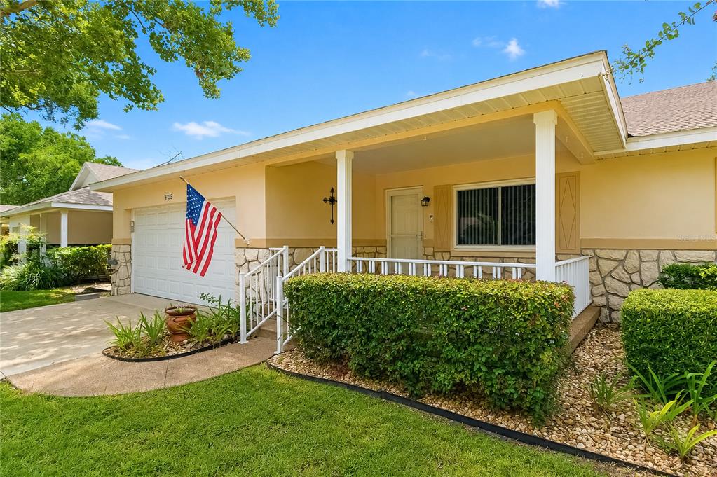 A single-story house with a covered porch, stone facade, and an American flag by the garage — 8702 SW 94TH STREET UNIT E, OCALA, FL