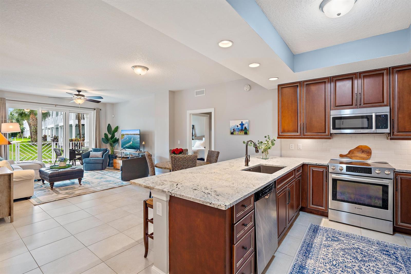 An open-concept kitchen with granite countertops overlooks a living area with a sliding glass door — 814 Bay Colony Drive S, Juno Beach FL 33408, JUNO BEACH, FL