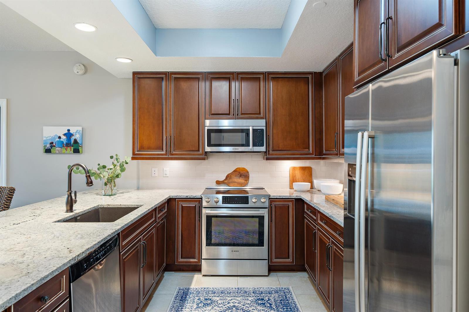 A kitchen features dark wood cabinets, stainless steel appliances, and granite countertops — 814 Bay Colony Drive S, Juno Beach FL 33408, JUNO BEACH, FL