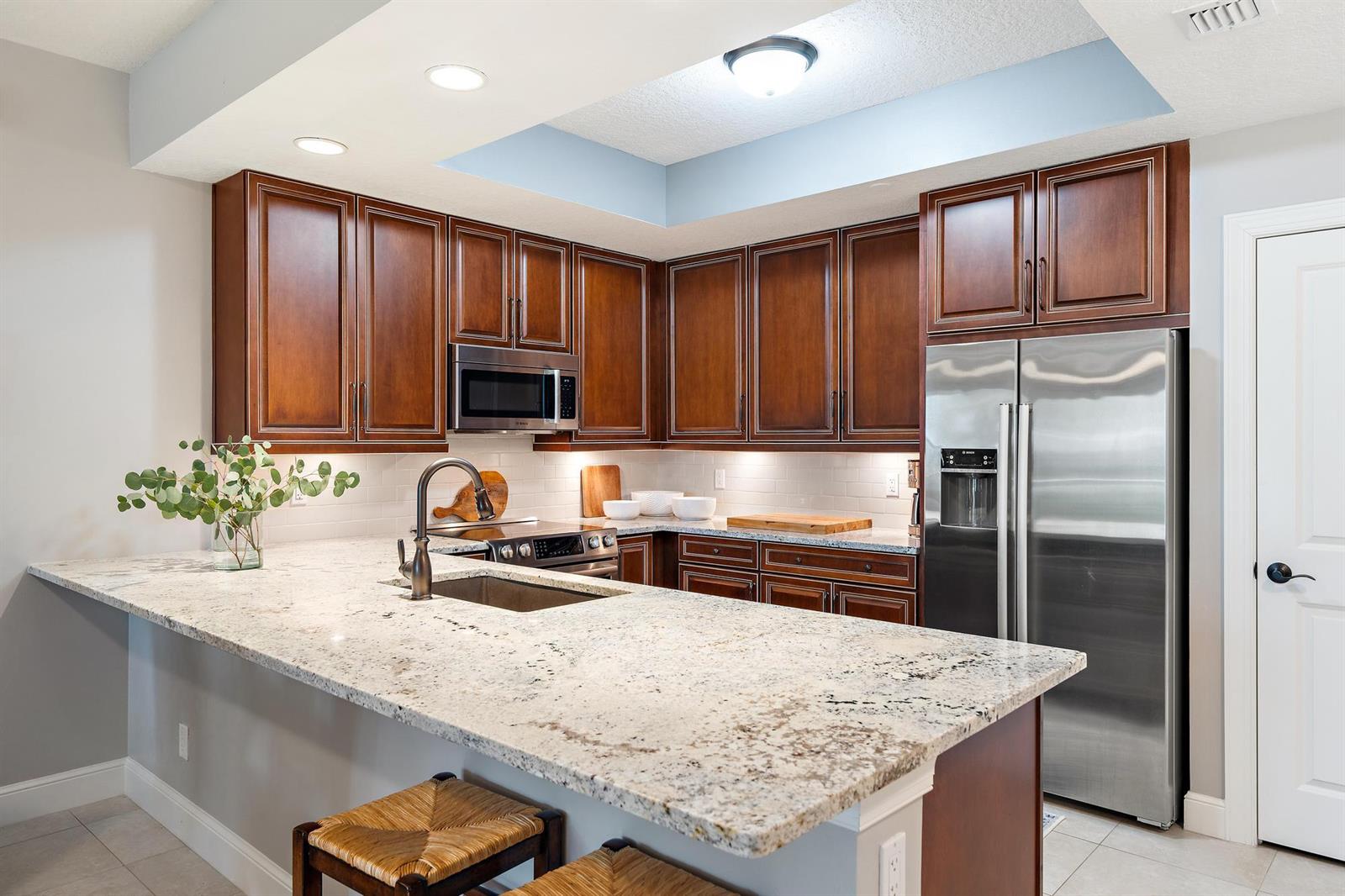 A kitchen features dark wood cabinets, granite countertops, stainless steel appliances, and a breakfast bar — 814 Bay Colony Drive S, Juno Beach FL 33408, JUNO BEACH, FL