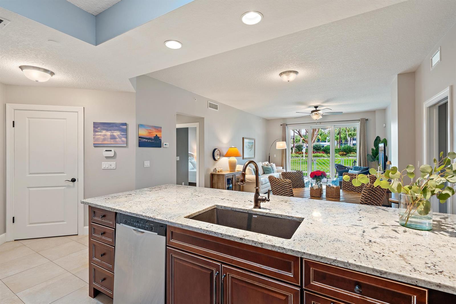 A kitchen island with a granite countertop and sink overlooks a living and dining area — 814 Bay Colony Drive S, Juno Beach FL 33408, JUNO BEACH, FL