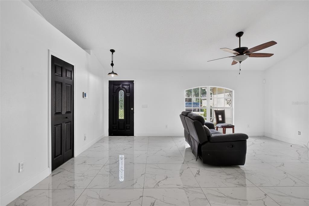 A living room features white walls, large marble-look floor tiles, a black door, and a sofa — 1865 15TH STREET, ORANGE CITY, FL