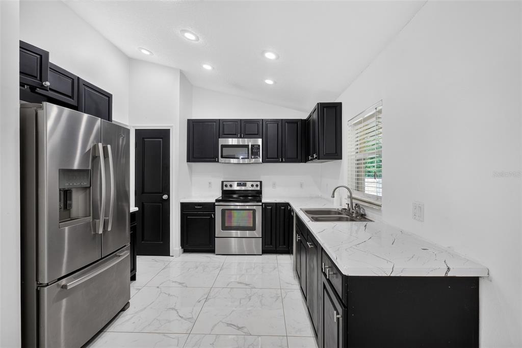 A kitchen features black cabinets, stainless steel appliances, and white marble-patterned countertops and flooring — 1865 15TH STREET, ORANGE CITY, FL