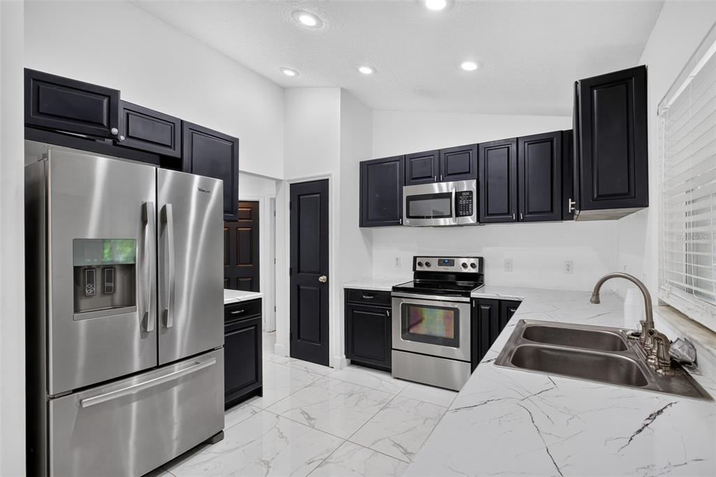 A kitchen features dark cabinets, stainless steel appliances, and white marble-patterned countertops and flooring — 1865 15TH STREET, ORANGE CITY, FL