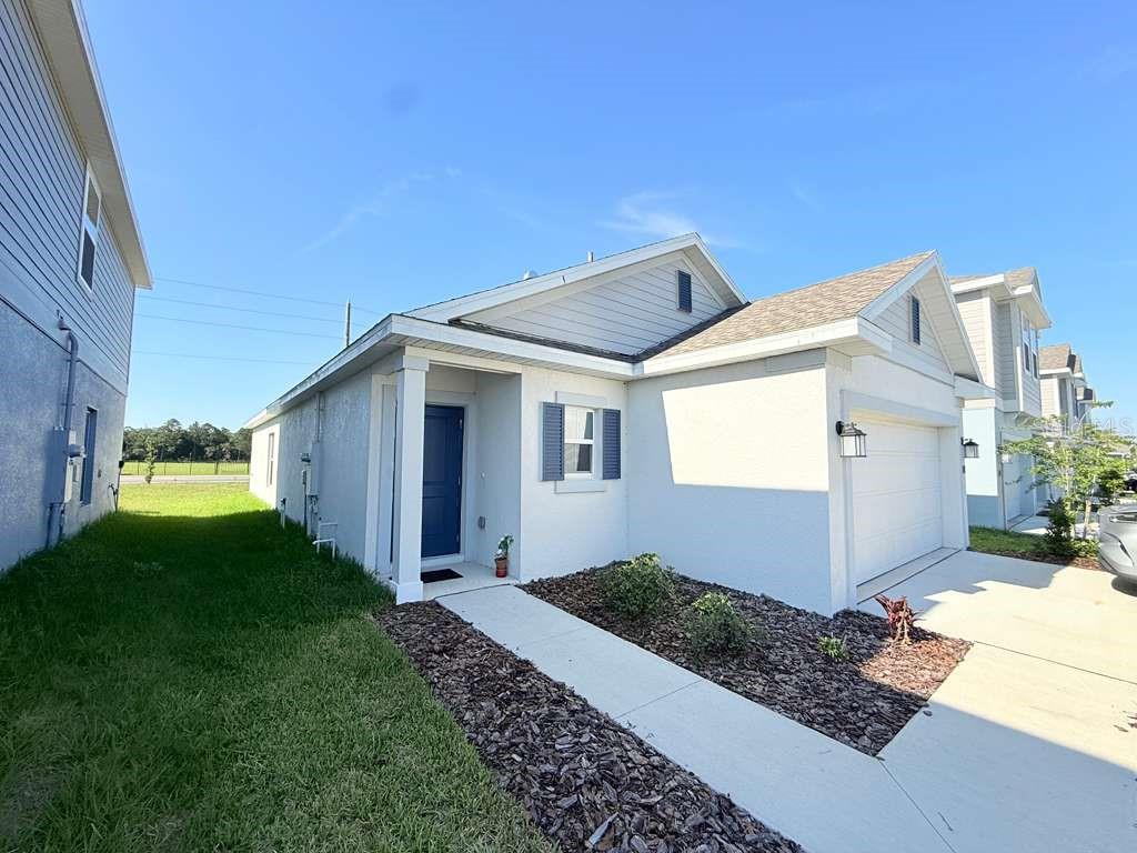 A single-story house with a white stucco exterior, blue front door, and a two-car garage — 1662 TEAGAN LANE, WINTER HAVEN, FL