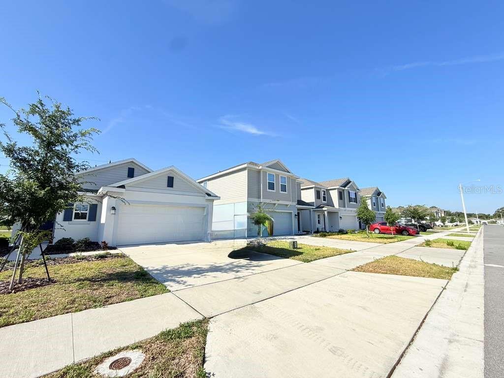 A row of suburban houses with light-colored siding and attached garages under a clear sky — 1662 TEAGAN LANE, WINTER HAVEN, FL