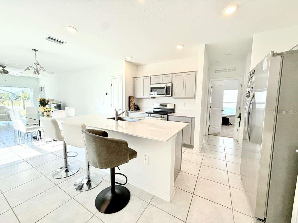 A modern kitchen features white cabinetry, a quartz island with bar stools, and tile flooring — 1662 TEAGAN LANE, WINTER HAVEN, FL