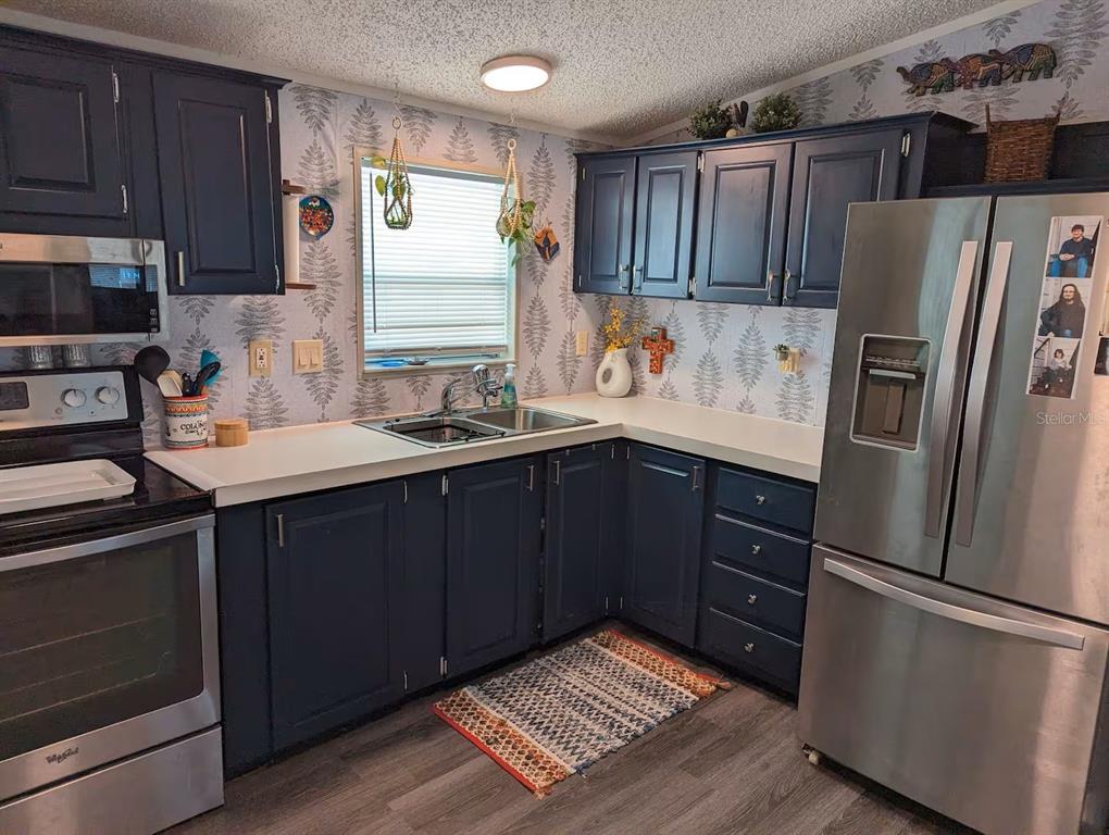 A kitchen features dark blue cabinets, stainless steel appliances, white countertops, and fern-patterned wallpaper — 12970 SPENCER STREET, FORT MYERS, FL