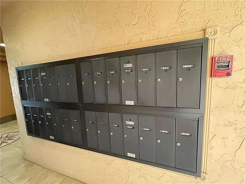 A wall-mounted bank of gray metal mailboxes is installed on a textured beige wall — 3001 W Rolling Hills # 608, Davie FL 33328, DAVIE, FL