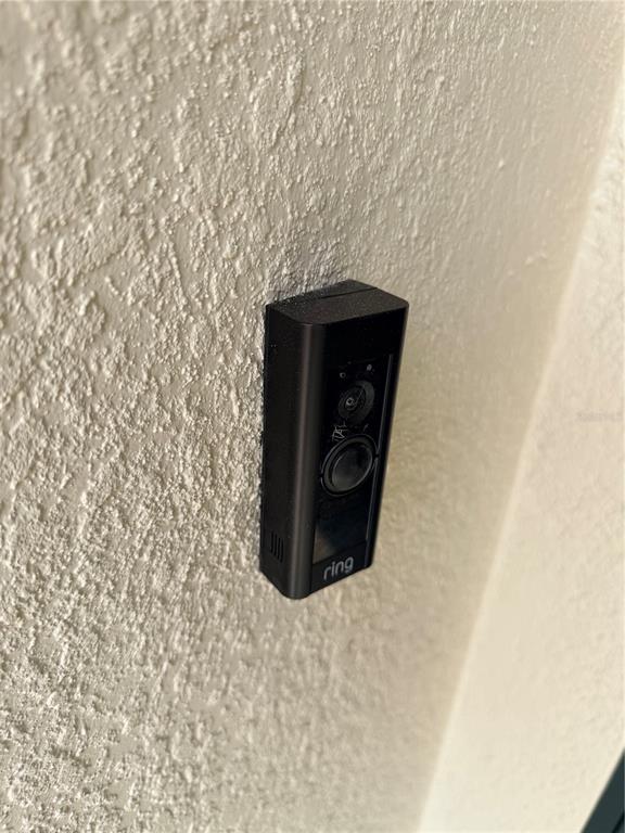 A black Ring video doorbell is mounted on a textured, off-white exterior wall — 16491 GLASSY LOCH LOOP, CLERMONT, FL