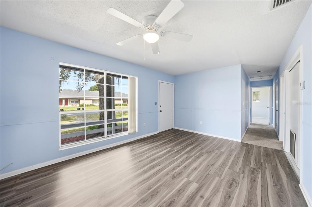 An empty room with light blue walls, wood-look flooring, a ceiling fan, and a large window — 704 N MANATEE AVENUE, ARCADIA, FL