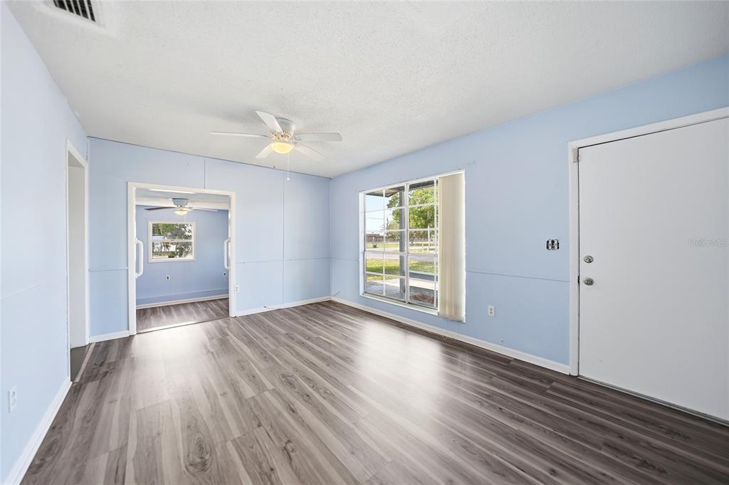 A living room with light blue walls, wood-look flooring, a ceiling fan, and a front door — 704 N MANATEE AVENUE, ARCADIA, FL