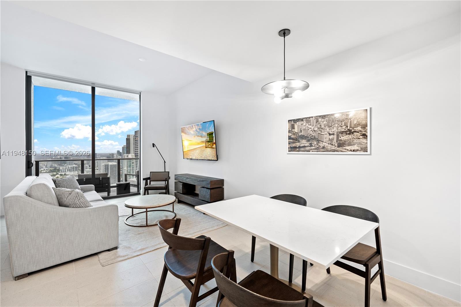 A modern living and dining area features a white table, sofa, and floor-to-ceiling windows — 159 NE 6th St # 5113, Miami FL 33132, MIAMI, FL