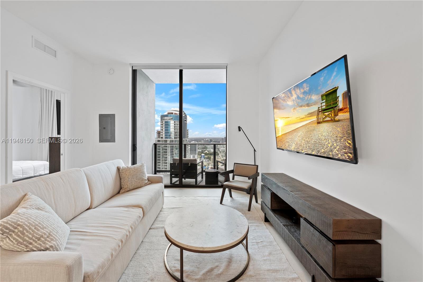 A modern living room features a beige sofa, a circular coffee table, and a wall-mounted television — 159 NE 6th St # 5113, Miami FL 33132, MIAMI, FL